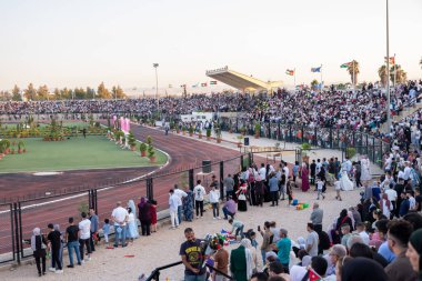 Stadyum sandalyelerinde izleyiciler mezuniyet kutlamalarını izliyorlar. Aileleri ve akrabaları için el sallıyorlar, onlar için seviniyorlar. (Jordan, 24 Temmuz 'da Ürdün Bilim ve Teknoloji Üniversitesi)