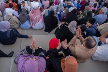 Arap Ailesi mezuniyet törenini izlerken elinde güller ve hediyelerle stadyum koltuklarından izliyor.