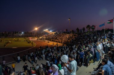 Stadyum sandalyelerinde izleyiciler mezuniyet kutlamalarını izliyorlar. Aileleri ve akrabaları için el sallıyorlar, onlar için seviniyorlar. (Jordan, 24 Temmuz 'da Ürdün Bilim ve Teknoloji Üniversitesi)