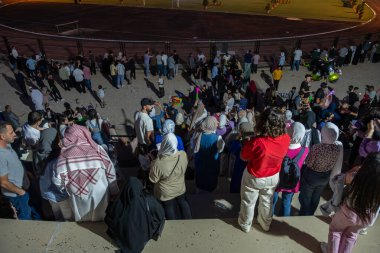 Stadyum sandalyelerinde izleyiciler mezuniyet kutlamalarını izliyorlar. Aileleri ve akrabaları için el sallıyorlar, onlar için seviniyorlar. (Jordan, 24 Temmuz 'da Ürdün Bilim ve Teknoloji Üniversitesi)