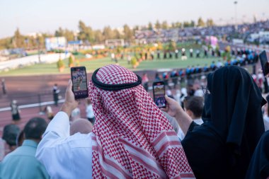 Arap Müslüman baba ve anne, üniversiteden mezun olduğu gün oğulları için fotoğraf çekiyorlar. Anne peçe takıyor ve tesettürlü, Ürdün 'lü baba kırmızı keffiyeh giyiyor.