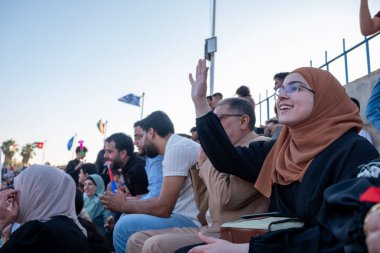 Arap kadın oğlunun mezuniyetini seyrediyor ve sahnede diplomasını alırken ona el sallıyor.