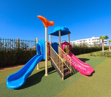 Ağaçlarla çevrili bir konut parkında renkli bir oyun alanı. Çocuklar modern ekipmanları seviyor, çocukluklarını somutlaştırıyorlar.