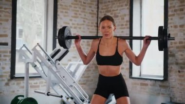 Spor salonunda halterle çömelmiş bir kadın. Spor meraklısı ağırlıklarla çömelme hareketi yapıyor. Güçlü kadın antrenmanda halter kaldırıyor. Spor salonunda halterle egzersiz yapan bir kadın. Kadın spor salonunda çekirdek egzersizi yapıyor. Spor salonundaki spor meraklısı.. 