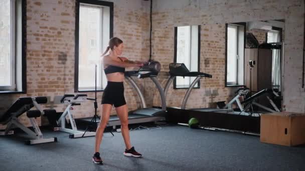 女人带着坚定的决心举起水壶 带水壶铃的体操锻炼 力量训练在行动 健身的重点与水壶的升降 在体育馆里做核心运动的女人 健身爱好者在健身房锻炼 — 图库视频影像