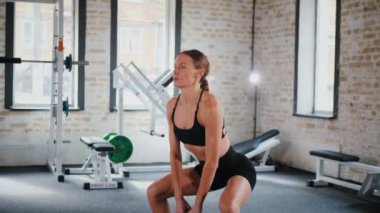 Kettlebell 'i kararlılıkla kaldıran kadın. Kettlebell 'le spor yapıyorum. Güç eğitimi iş başında. Kettlebell kaldırma ile fitness odağı. Kadın spor salonunda çekirdek egzersizi yapıyor. Spor salonundaki spor meraklısı.. 