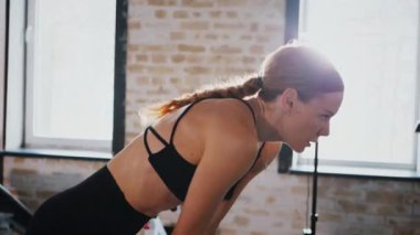 Atletik giyinmiş genç bir kadın parlak bir spor salonunda dikiliyor. Spor salonunda kararlı görünen bir kadın. Spor salonundaki antrenmana ara veren zinde bir kadın. Spor salonunda spor aletlerinin önünde poz veren kendine güvenen bir kadın.. 