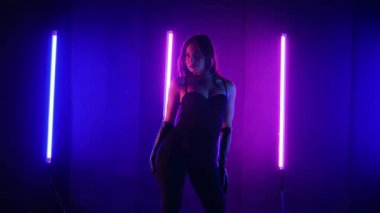 Neon ışıklarının altında dans eden kadın silueti. Canlı neon ışıklı dans pisti ve hareket halindeki bir kadın. Karanlık odada neon parıltısıyla enerjik bir dans gösterisi. Kendinden geçmiş kadın dansçı. Siyah elbiseli zarif bayan parlak neon ışıkların önünde poz veriyor..