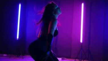 Neon ışıklarının altında dans eden kadın silueti. Canlı neon ışıklı dans pisti ve hareket halindeki bir kadın. Karanlık odada neon parıltısıyla enerjik bir dans gösterisi. Kendinden geçmiş kadın dansçı. Siyah elbiseli zarif bayan parlak neon ışıkların önünde poz veriyor..