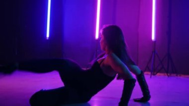 Neon ışıklarının altında dans eden kadın silueti. Canlı neon ışıklı dans pisti ve hareket halindeki bir kadın. Karanlık odada neon parıltısıyla enerjik bir dans gösterisi. Kendinden geçmiş kadın dansçı. Siyah elbiseli zarif bayan parlak neon ışıkların önünde poz veriyor..