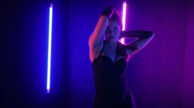 Neon ışıklarının altında dans eden kadın silueti. Canlı neon ışıklı dans pisti ve hareket halindeki bir kadın. Karanlık odada neon parıltısıyla enerjik bir dans gösterisi. Kendinden geçmiş kadın dansçı. Siyah elbiseli zarif bayan parlak neon ışıkların önünde poz veriyor..