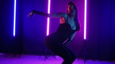 Neon ışıklarının altında dans eden kadın silueti. Canlı neon ışıklı dans pisti ve hareket halindeki bir kadın. Karanlık odada neon parıltısıyla enerjik bir dans gösterisi. Kendinden geçmiş kadın dansçı. Siyah elbiseli zarif bayan parlak neon ışıkların önünde poz veriyor..