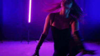 Neon ışıklarının altında dans eden kadın silueti. Canlı neon ışıklı dans pisti ve hareket halindeki bir kadın. Karanlık odada neon parıltısıyla enerjik bir dans gösterisi. Kendinden geçmiş kadın dansçı. Siyah elbiseli zarif bayan parlak neon ışıkların önünde poz veriyor..