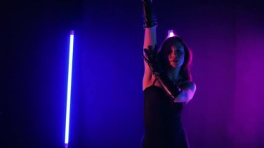 Neon ışıklarının altında dans eden kadın silueti. Canlı neon ışıklı dans pisti ve hareket halindeki bir kadın. Karanlık odada neon parıltısıyla enerjik bir dans gösterisi. Kendinden geçmiş kadın dansçı. Siyah elbiseli zarif bayan parlak neon ışıkların önünde poz veriyor..