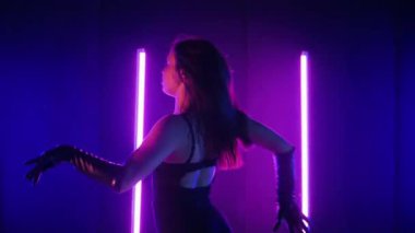 Neon ışıklarının altında dans eden kadın silueti. Canlı neon ışıklı dans pisti ve hareket halindeki bir kadın. Karanlık odada neon parıltısıyla enerjik bir dans gösterisi. Kendinden geçmiş kadın dansçı. Siyah elbiseli zarif bayan parlak neon ışıkların önünde poz veriyor..
