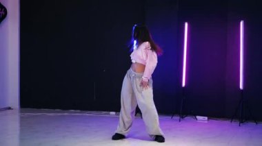 Renkli neon ışıkların önünde dans eden kız. Enerjik kız caz funk, hip hop, canlı neon fon ile dans ediyor. Genç kadın neon ışığı altında zarifçe hareket ediyor. Neon ışıkları kızın neşeli dansını aydınlatır.
