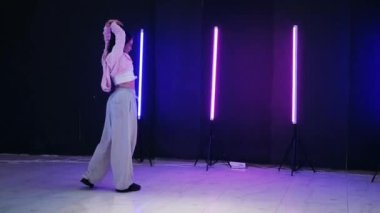 Renkli neon ışıkların önünde dans eden kız. Enerjik kız caz funk, hip hop, canlı neon fon ile dans ediyor. Genç kadın neon ışığı altında zarifçe hareket ediyor. Neon ışıkları kızın neşeli dansını aydınlatır.