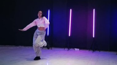 Renkli neon ışıkların önünde dans eden kız. Enerjik kız caz funk, hip hop, canlı neon fon ile dans ediyor. Genç kadın neon ışığı altında zarifçe hareket ediyor. Neon ışıkları kızın neşeli dansını aydınlatır.
