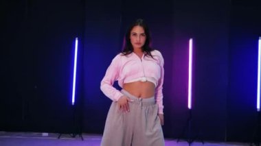 Renkli neon ışıkların önünde dans eden kız. Enerjik kız caz funk, hip hop, canlı neon fon ile dans ediyor. Genç kadın neon ışığı altında zarifçe hareket ediyor. Neon ışıkları kızın neşeli dansını aydınlatır.