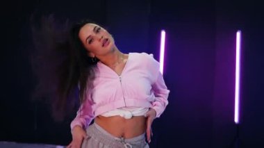 Renkli neon ışıkların önünde dans eden kız. Enerjik kız caz funk, hip hop, canlı neon fon ile dans ediyor. Genç kadın neon ışığı altında zarifçe hareket ediyor. Neon ışıkları kızın neşeli dansını aydınlatır.