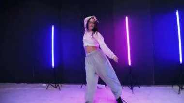 Renkli neon ışıkların önünde dans eden kız. Enerjik kız caz funk, hip hop, canlı neon fon ile dans ediyor. Genç kadın neon ışığı altında zarifçe hareket ediyor. Neon ışıkları kızın neşeli dansını aydınlatır.