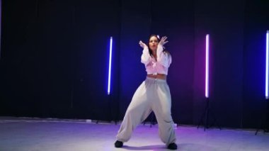Renkli neon ışıkların önünde dans eden kız. Enerjik kız caz funk, hip hop, canlı neon fon ile dans ediyor. Genç kadın neon ışığı altında zarifçe hareket ediyor. Neon ışıkları kızın neşeli dansını aydınlatır.