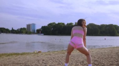 Sahilde dans eden seksi kız. Güzel bir kadın kalçasıyla kumda dans eder. Bikinili seksi kadın. Bikinili genç bir kadın kumların üzerinde enerjik bir dans ediyor..