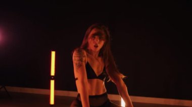 Sexy woman dancing a seductive dance. A dancer girl with a big ass dances erotically in a dark hall. Twerk, high heels, striptease. Sultry woman in lingerie posing in front of a soft light. Sensual pose in lingerie against a glowing backdrop. 