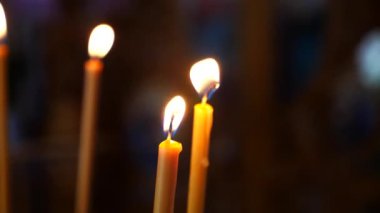 Loş bir kilisede mum yakmak. İbadet yerinde mumların sıcaklığı. Mumlar kutsal bir yerde parlıyor. Mumları yakmak huzurlu bir atmosfer yaratıyor.
