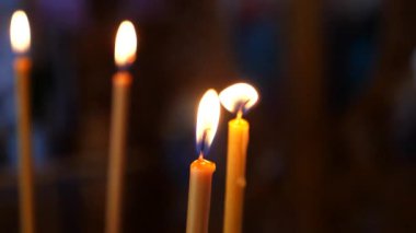 Loş bir kilisede mum yakmak. İbadet yerinde mumların sıcaklığı. Mumlar kutsal bir yerde parlıyor. Mumları yakmak huzurlu bir atmosfer yaratıyor.