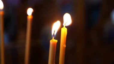 Loş bir kilisede mum yakmak. İbadet yerinde mumların sıcaklığı. Mumlar kutsal bir yerde parlıyor. Mumları yakmak huzurlu bir atmosfer yaratıyor.