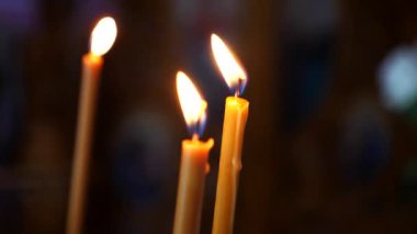 Loş bir kilisede mum yakmak. İbadet yerinde mumların sıcaklığı. Mumlar kutsal bir yerde parlıyor. Mumları yakmak huzurlu bir atmosfer yaratıyor.