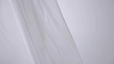 Beyaz şeffaf kumaş rüzgarda dalgalanıyor. Parlak bir stüdyoda uzun beyaz perdeler. Rüzgarda savrulan saf beyaz perdeler. Ağır çekim. Görüntüler. Güneşli bir odada beyaz bir perde yükseliyor. Yumuşak, dalgalı beyaz perde Sakin bir ortamda. 