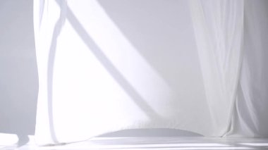 Beyaz şeffaf kumaş rüzgarda dalgalanıyor. Parlak bir stüdyoda uzun beyaz perdeler. Rüzgarda savrulan saf beyaz perdeler. Ağır çekim. Görüntüler. Güneşli bir odada beyaz bir perde yükseliyor. Yumuşak, dalgalı beyaz perde Sakin bir ortamda. 