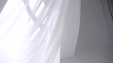 Beyaz şeffaf kumaş rüzgarda dalgalanıyor. Parlak bir stüdyoda uzun beyaz perdeler. Rüzgarda savrulan saf beyaz perdeler. Ağır çekim. Görüntüler. Güneşli bir odada beyaz bir perde yükseliyor. Yumuşak, dalgalı beyaz perde Sakin bir ortamda. 