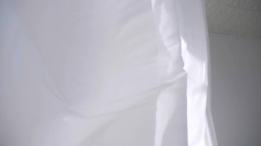 Beyaz şeffaf kumaş rüzgarda dalgalanıyor. Parlak bir stüdyoda uzun beyaz perdeler. Rüzgarda savrulan saf beyaz perdeler. Ağır çekim. Görüntüler. Güneşli bir odada beyaz bir perde yükseliyor. Yumuşak, dalgalı beyaz perde Sakin bir ortamda. 