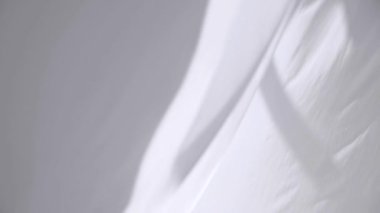 Beyaz şeffaf kumaş rüzgarda dalgalanıyor. Parlak bir stüdyoda uzun beyaz perdeler. Rüzgarda savrulan saf beyaz perdeler. Ağır çekim. Görüntüler. Güneşli bir odada beyaz bir perde yükseliyor. Yumuşak, dalgalı beyaz perde Sakin bir ortamda. 