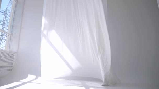 白色透明的织物在风中飘扬 明亮的演播室里有长长的白色窗帘 白色的窗帘在风中飘扬 慢动作 一道白色的窗帘在阳光明媚的房间里飘扬 在宁静的环境中 柔和的 波涛汹涌的白色帷幕 — 图库视频影像
