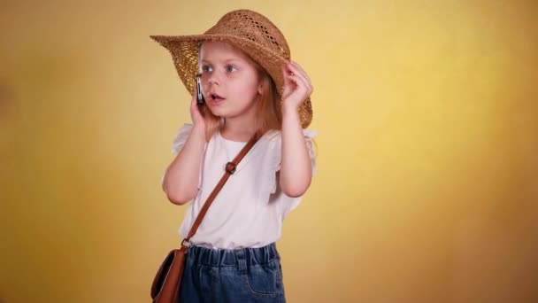 帽子をかぶったかわいい女の子が電話で笑う ストロー帽子の小さな女の子は 興奮して電話で話しています 太陽の下の若い女の子は携帯電話でチャットします ストロー帽子の子供は 活発な電話会話を持っています かわいい — ストック動画
