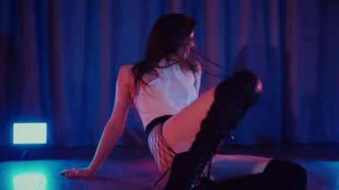 Yüksek topuklularla dans eden seksi kadın. Bir dansçı kız karanlık bir salonda erotik bir şekilde dans eder. Twerk, yüksek topuklar, striptiz, baştan çıkarıcı bir dans. Balık ağı çoraplı baştan çıkarıcı kadın yerde poz veriyor. Balık ağı çoraplı kadın yerde kendine güvenini sergiliyor.. 