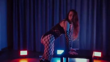 Dans eden seksi kadın twerk. Bir dansçı kız karanlık bir salonda erotik bir şekilde dans eder. Twerk, yüksek topuklu ayakkabı, striptiz, baştan çıkarıcı bir dans. Balık ağı çoraplı bir kadın yerde şehvetli bir poz veriyor. Ağ çoraplı zarif bayan yerde tarzını sergiliyor..