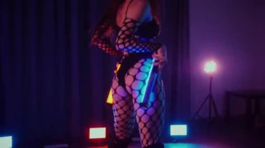 Dans eden seksi kadın twerk. Bir dansçı kız karanlık bir salonda erotik bir şekilde dans eder. Twerk, yüksek topuklu ayakkabı, striptiz, baştan çıkarıcı bir dans. Balık ağı çoraplı bir kadın yerde şehvetli bir poz veriyor. Ağ çoraplı zarif bayan yerde tarzını sergiliyor..
