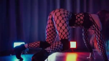 Dans eden seksi kadın twerk. Bir dansçı kız karanlık bir salonda erotik bir şekilde dans eder. Twerk, yüksek topuklu ayakkabı, striptiz, baştan çıkarıcı bir dans. Balık ağı çoraplı bir kadın yerde şehvetli bir poz veriyor. Ağ çoraplı zarif bayan yerde tarzını sergiliyor..