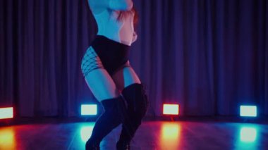 Yüksek topuklularla dans eden seksi kadın. Yavaş çekim. Bir dansçı kız karanlık bir salonda erotik bir şekilde dans eder. Twerk, yüksek topuklar, striptiz, baştan çıkarıcı bir dans. Atmosferik renkli ışık, kulüp, sahne. Balık ağı çoraplı baştan çıkarıcı kadın yerde poz veriyor.. 