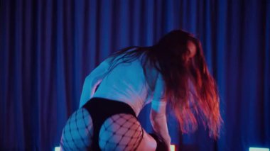 Yüksek topuklularla dans eden seksi kadın. Yavaş çekim. Bir dansçı kız karanlık bir salonda erotik bir şekilde dans eder. Twerk, yüksek topuklar, striptiz, baştan çıkarıcı bir dans. Atmosferik renkli ışık, kulüp, sahne. Balık ağı çoraplı baştan çıkarıcı kadın yerde poz veriyor.. 