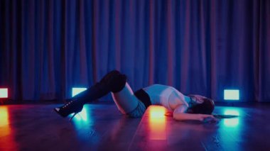Yüksek topuklularla dans eden seksi kadın. Yavaş çekim. Bir dansçı kız karanlık bir salonda erotik bir şekilde dans eder. Twerk, yüksek topuklar, striptiz, baştan çıkarıcı bir dans. Atmosferik renkli ışık, kulüp, sahne. Balık ağı çoraplı baştan çıkarıcı kadın yerde poz veriyor.. 