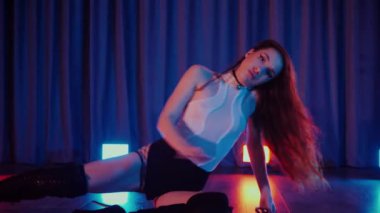 Yüksek topuklularla dans eden seksi kadın. Yavaş çekim. Bir dansçı kız karanlık bir salonda erotik bir şekilde dans eder. Twerk, yüksek topuklar, striptiz, baştan çıkarıcı bir dans. Atmosferik renkli ışık, kulüp, sahne. Balık ağı çoraplı baştan çıkarıcı kadın yerde poz veriyor.. 