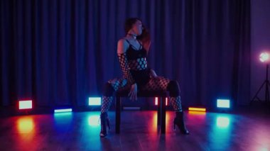 Dans eden seksi kadın twerk. Bir dansçı kız karanlık bir salonda erotik bir şekilde dans eder. Yavaş çekim. Twerk, yüksek topuklar, striptiz, baştan çıkarıcı bir dans. Atmosferik renkli ışık, kulüp, sahne. Balık ağı çoraplı bir kadın yerde boğucu bir poz veriyor..