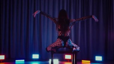 Dans eden seksi kadın twerk. Bir dansçı kız karanlık bir salonda erotik bir şekilde dans eder. Yavaş çekim. Twerk, yüksek topuklar, striptiz, baştan çıkarıcı bir dans. Atmosferik renkli ışık, kulüp, sahne. Balık ağı çoraplı bir kadın yerde boğucu bir poz veriyor..