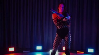Elinde fenerlerle dans eden seksi bir kadın. Bir dansçı kız karanlık bir salonda erotik bir şekilde dans eder. Yavaş çekim. Twerk, yüksek topuklar, striptiz, baştan çıkarıcı bir dans. Balık ağı çoraplı bir kadın ahşap zeminde boğucu bir poz veriyor..